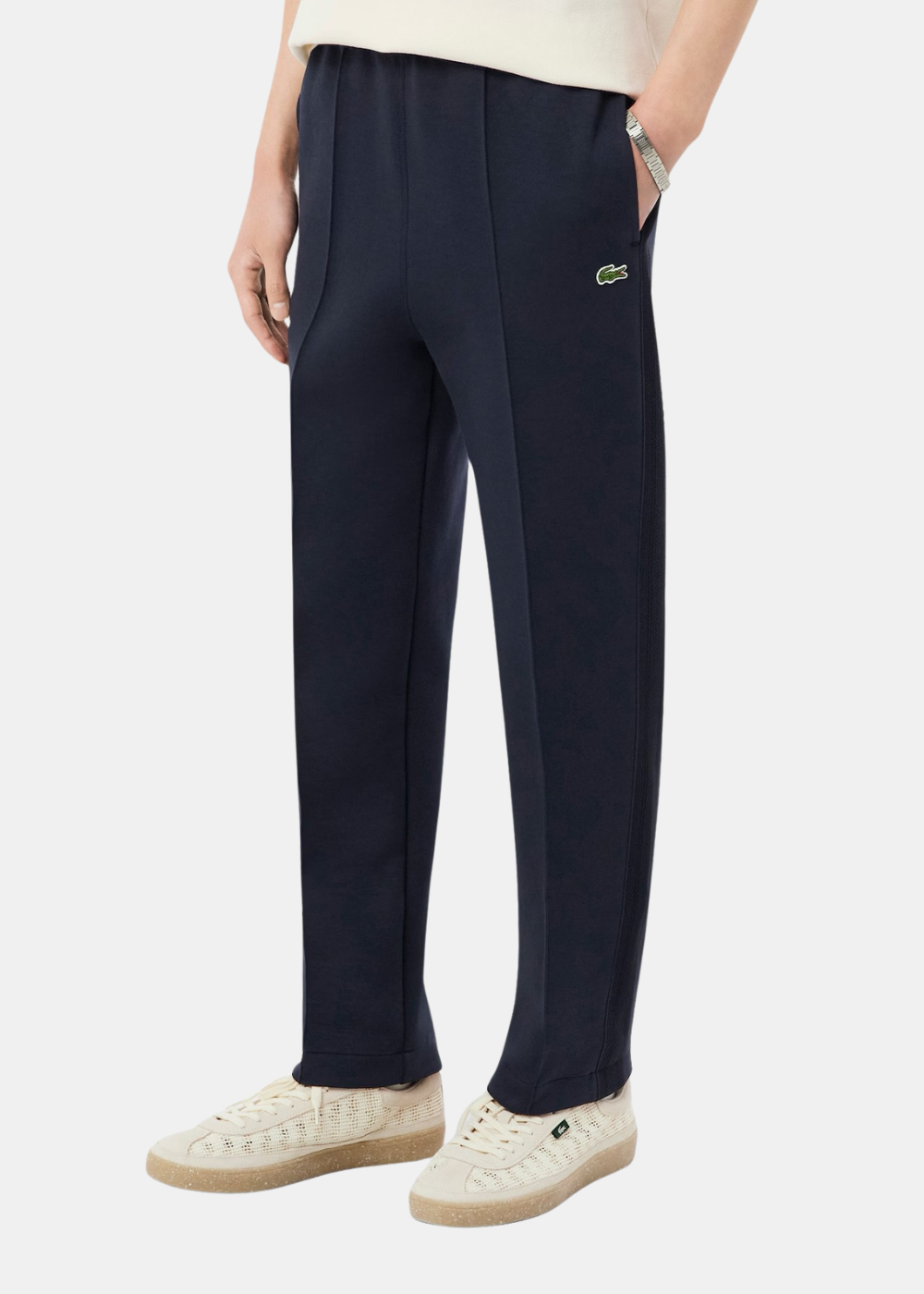 Zoom sur la jambe du pantalon de survêtement Lacoste marine porté avec des baskets blanches.