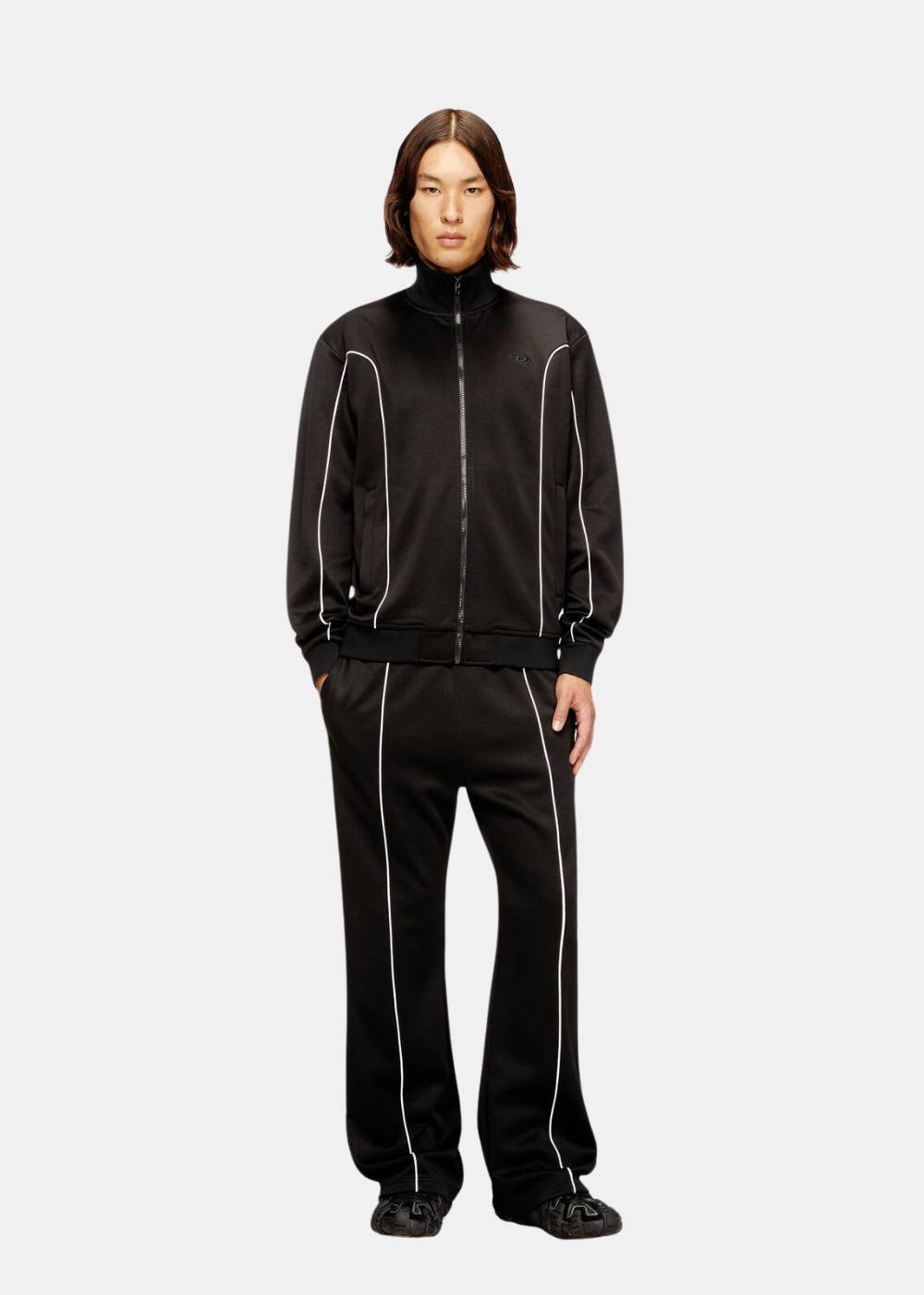 Silhouette complète du mannequin portant le pantalon de survêtement noir Diesel avec la veste assortie et des baskets.