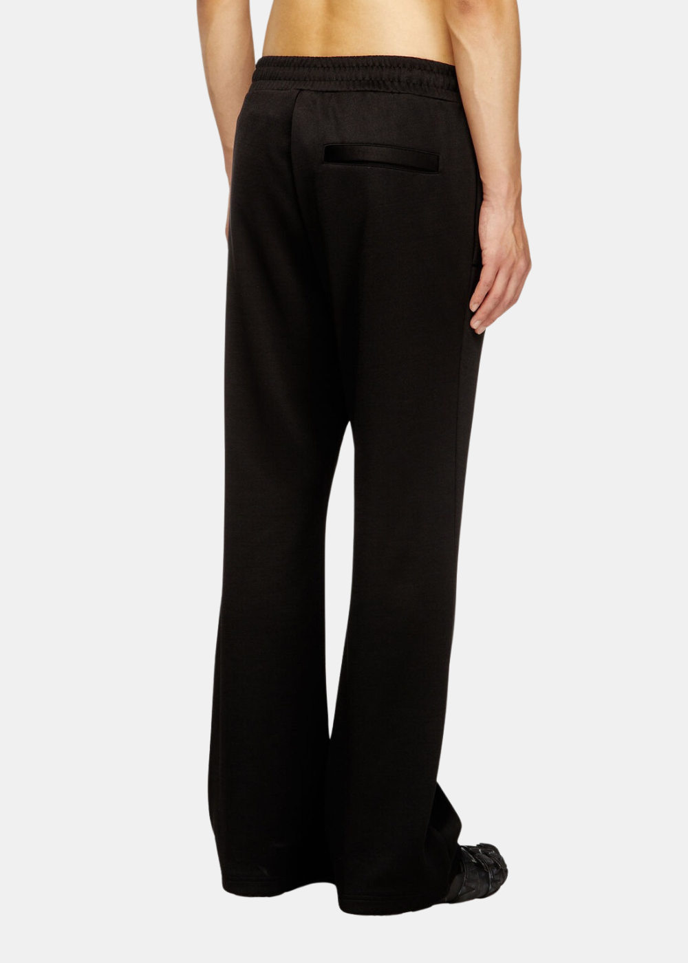 Zoom de trois-quarts dos sur un mannequin portant le pantalon de survêtement noir Diesel avec poche passepoilée.