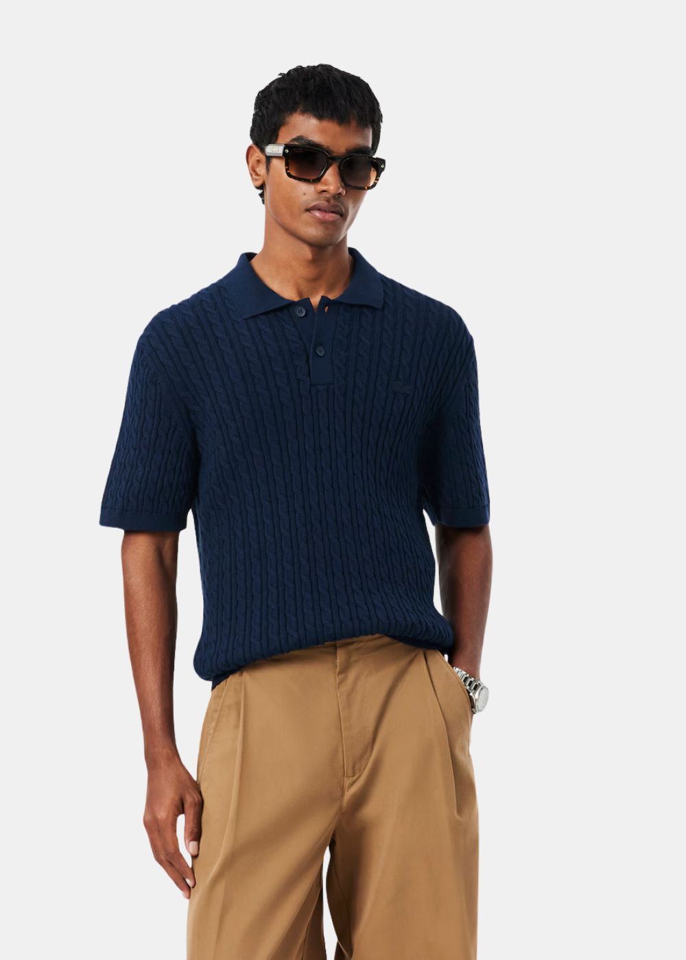Mannequin portant le polo Lacoste bleu marine en maille torsadée associé à un pantalon camel.