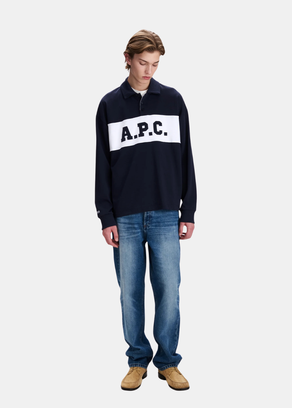 Polo bleu marine A.P.C. Alexis à manches longues porté par un mannequin de face, associé à un jean bleu délavé et des chaussures en daim beige.
