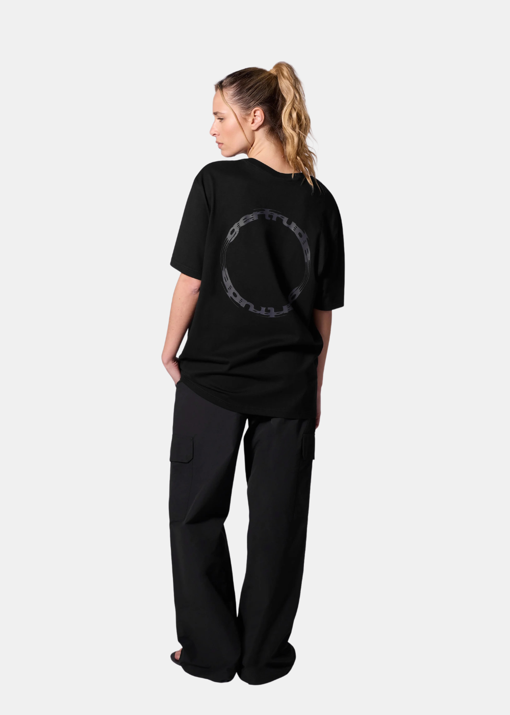 Mannequin femme de dos portant le t-shirt noir Gertrude imprimé, un pantalon cargo noir large, sur fond uni blanc.