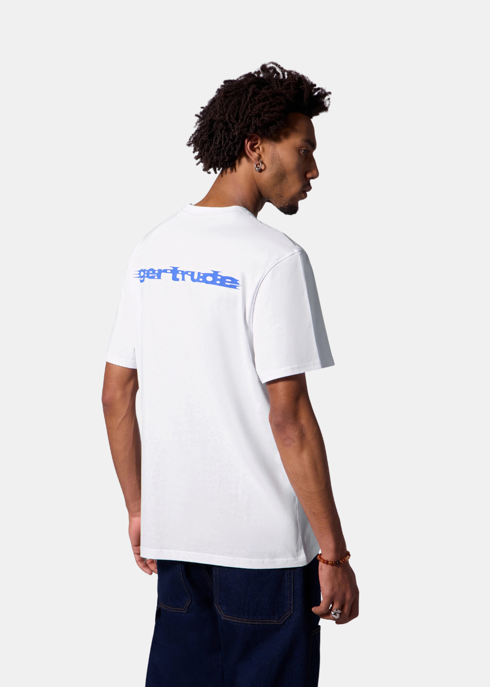 Mannequin homme de trois-quarts dos portant le t-shirt blanc Gertrude, un jean brut et des bijoux, sur fond uni blanc.