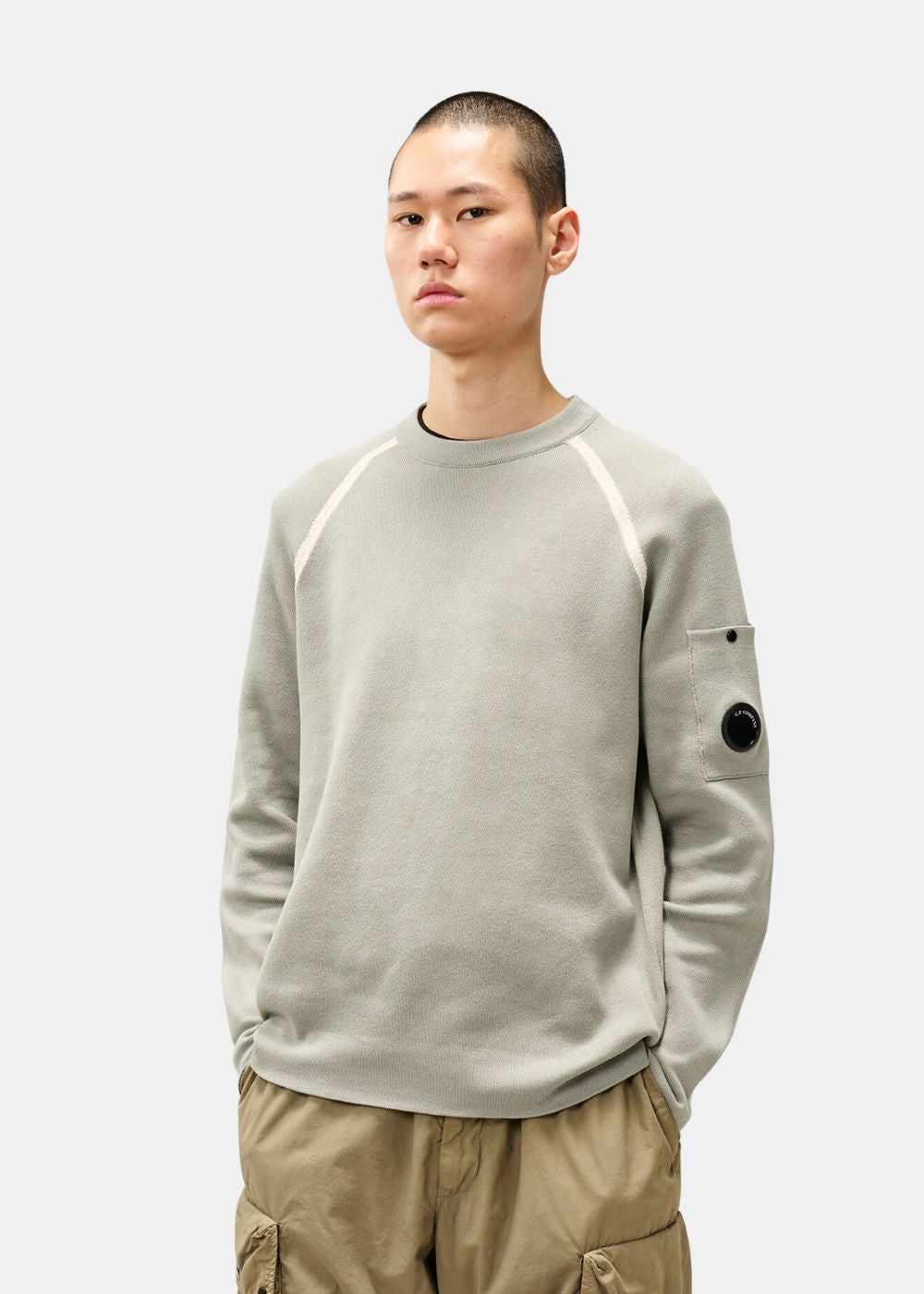 Plan moyen du mannequin portant le pull C.P. Company gris avec lentille NFC mate sur le bras.