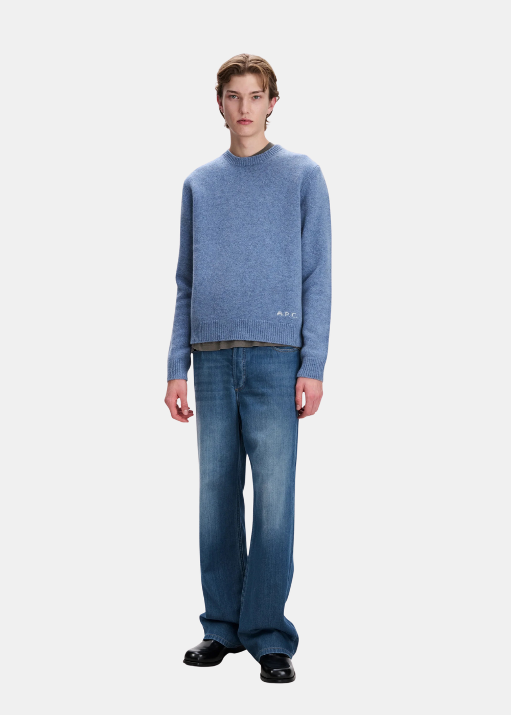 Mannequin homme de face en pied portant le pull bleu chiné A.P.C. avec un t-shirt dépassant, un jean bleu délavé coupe droite et des chaussures en cuir noir