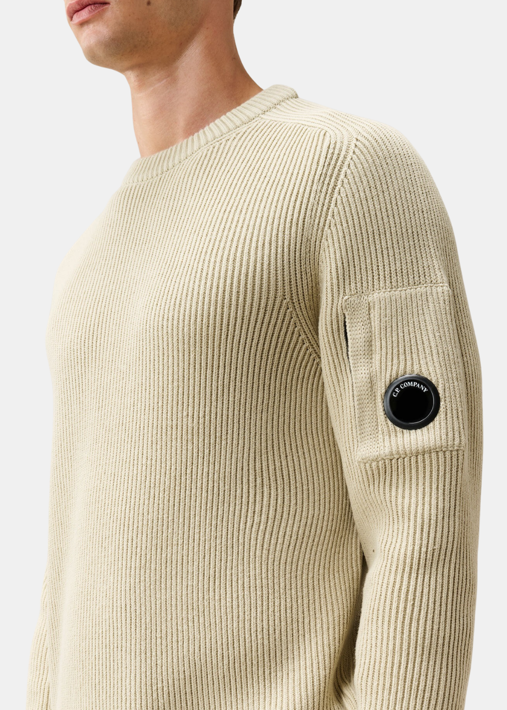 Gros plan sur le détail verre Lens noir C.P. Company sur la poche zippée de la manche gauche du pull beige