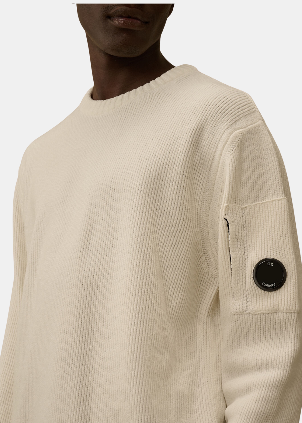 Gros plan sur le pull CP Company en coton chenille blanc et la lentille signature sur la manche.