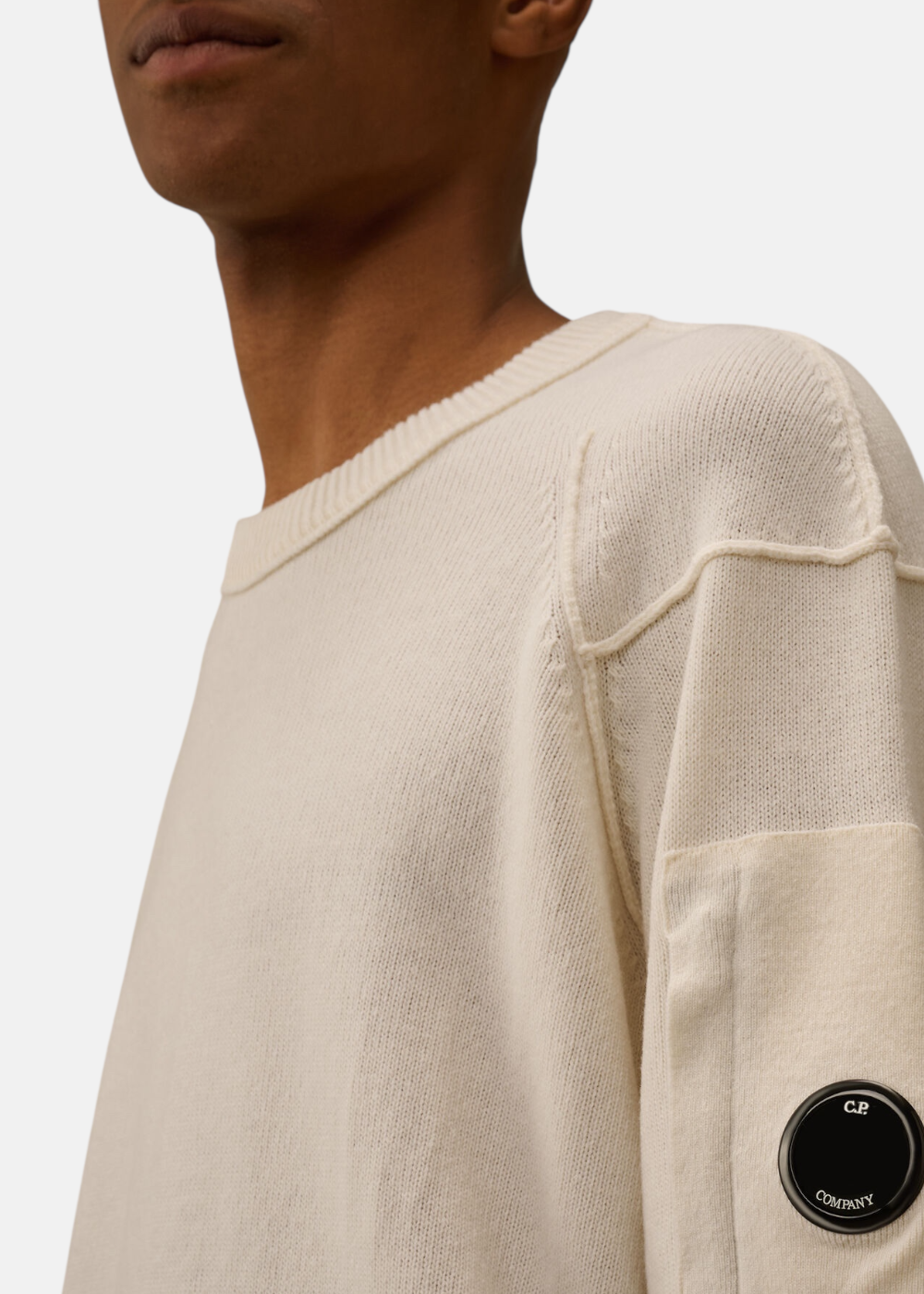 Gros plan sur le patch C.P. Company avec lentille noire et le tricot en laine Lambswool GRS.