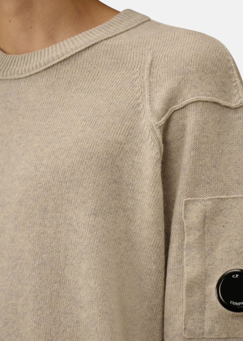 Gros plan sur le pull Lambswool GRS clair avec manchon et lentille C.P. Company.