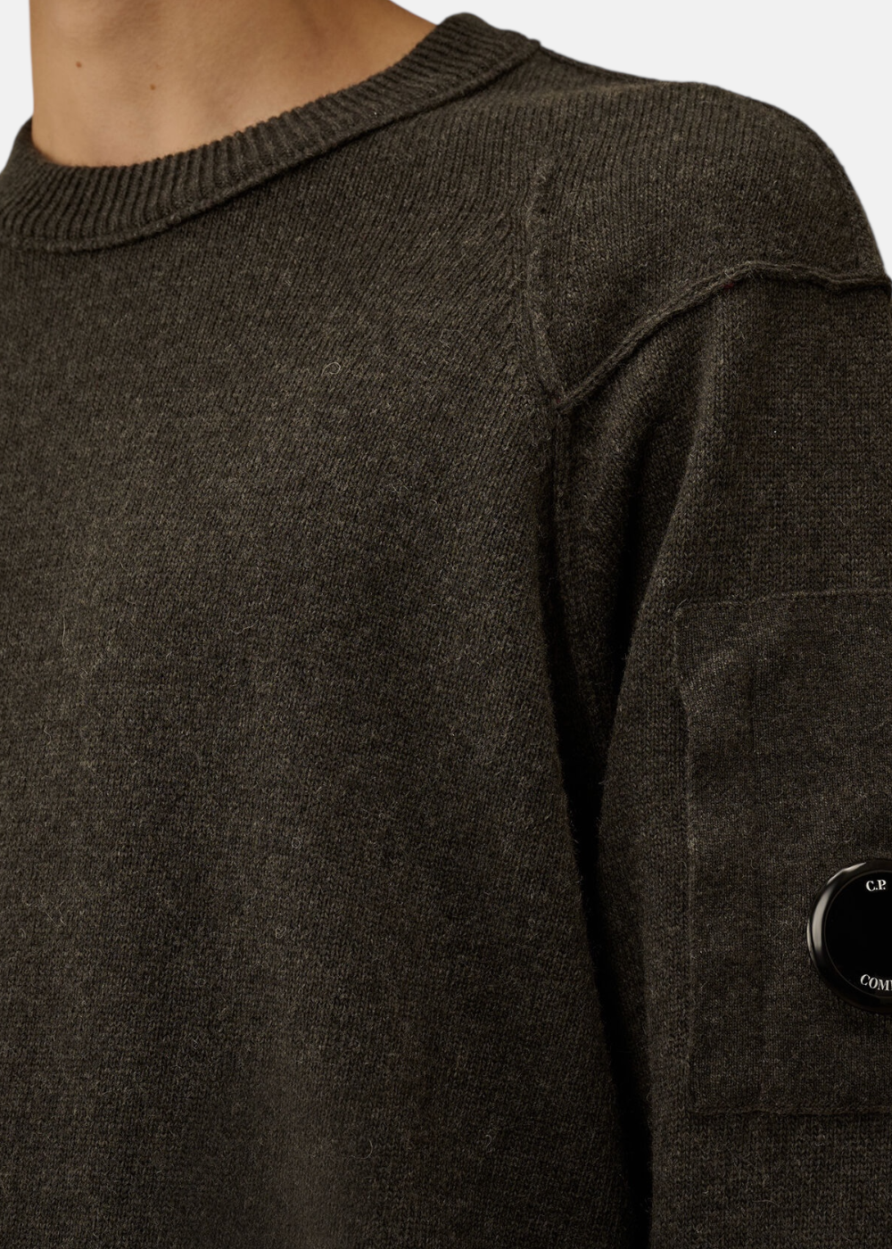 Gros plan sur le patch lentille C.P. Company sur le pull en laine Lambswool gris.