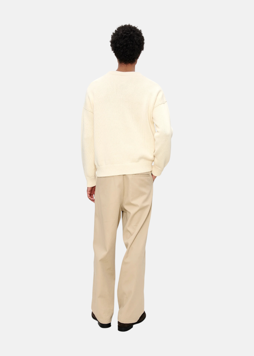 Mannequin de dos portant un pull crème A.P.C. et un pantalon large beige, look complet minimaliste.
