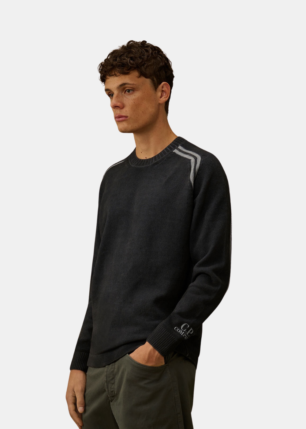 Mannequin homme de trois-quarts face portant le pull en chenille marine C.P. Company, montrant le détail des bandes grises sur l'épaule et l'inscription blanche C.P. Company sur la manche
