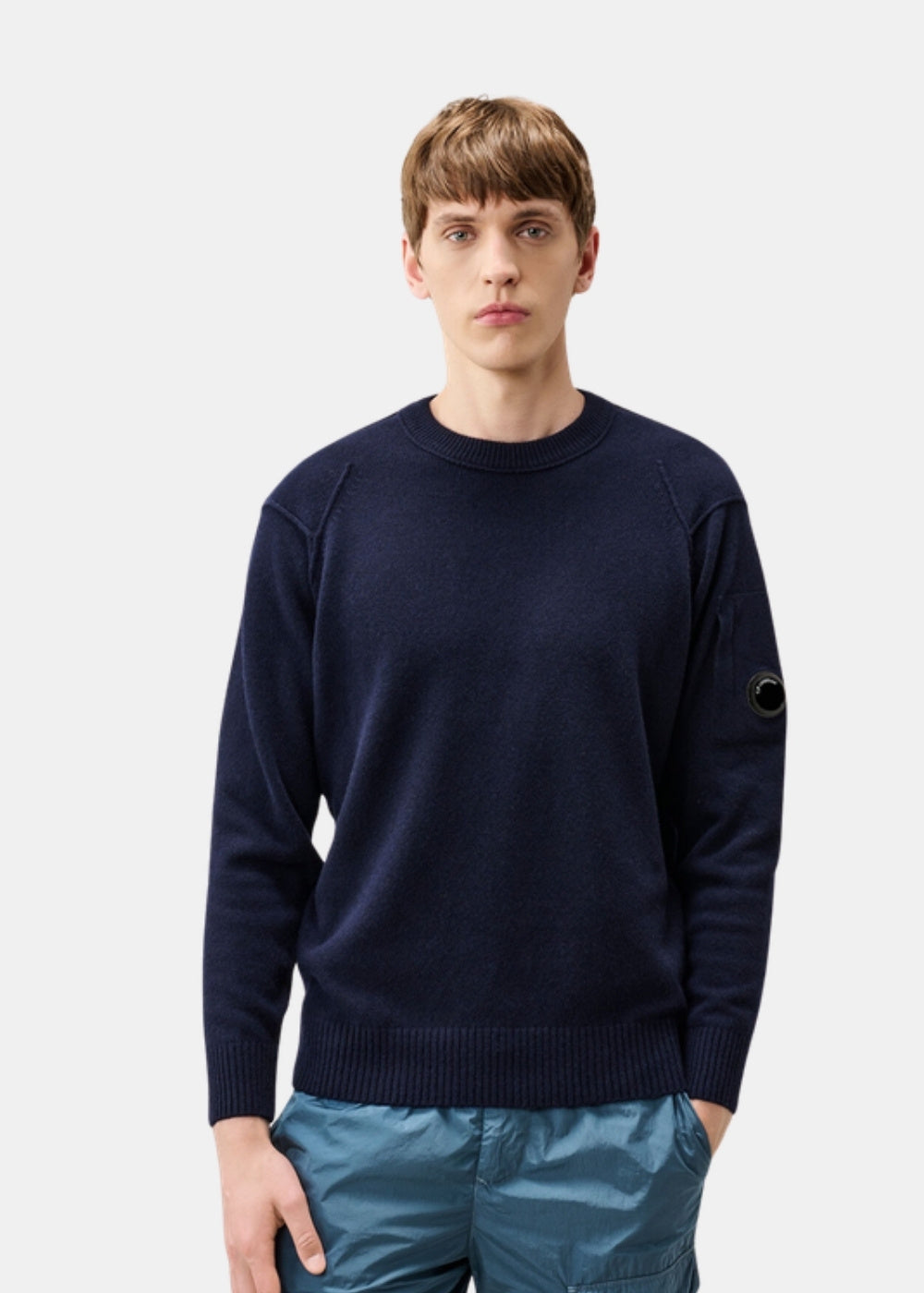 Porté de face d'un pull marine C.P. Company en laine d'agneau, col rond côtelé, coupe classique et badge manche.