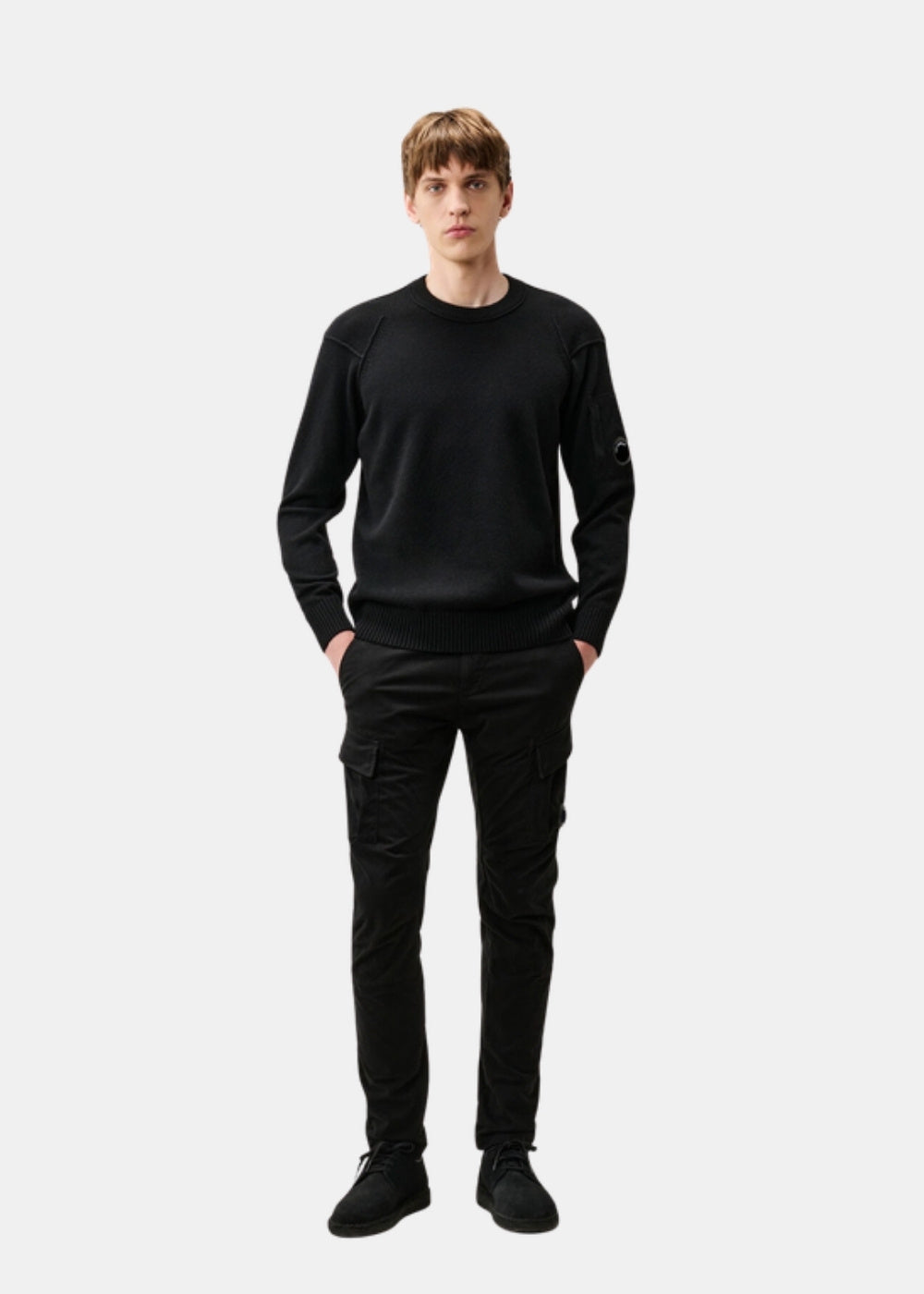 Porté en pied d'un pull noir C.P. Company en Lambswool associé à un pantalon cargo noir et des chaussures sombres.
