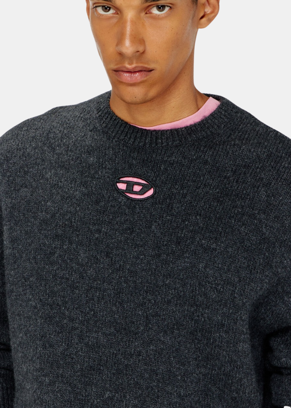 Gros plan sur le logo Oval D rose brodé au niveau du col du pull en maille noir Diesel