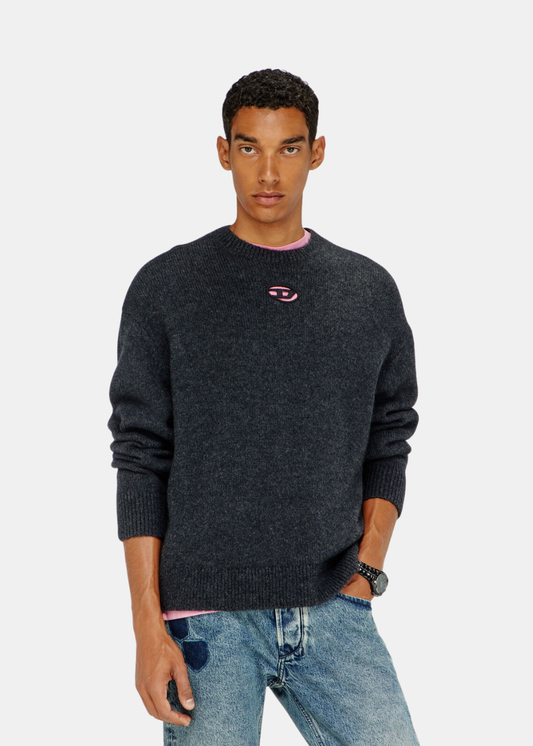 Mannequin homme de face portant le pull en maille noir Diesel avec logo Oval D rose et col t-shirt rose apparent