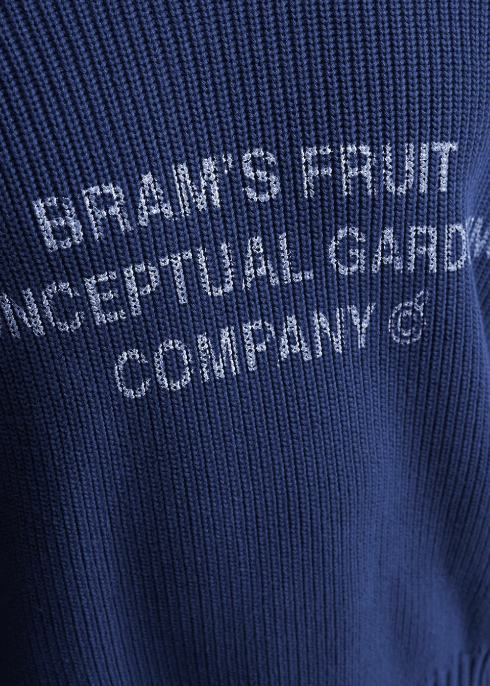 Zoom sur le lettrage blanc Bram's Fruit Conceptual Gardening Company sur la maille tricotée bleu marine.