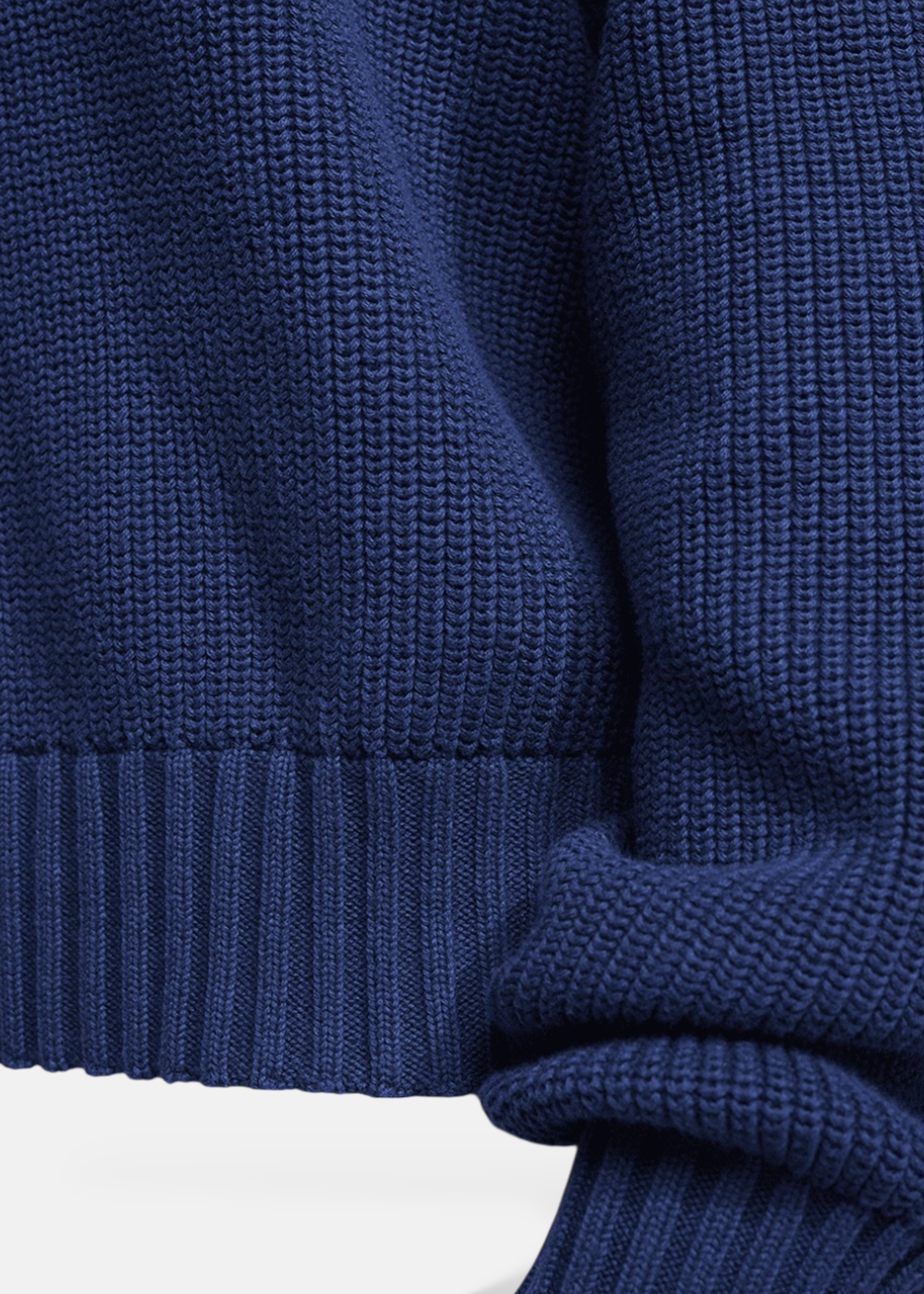 Gros plan sur la texture de la maille de coton bleu marine et les finitions bord-côte à la taille du pull.