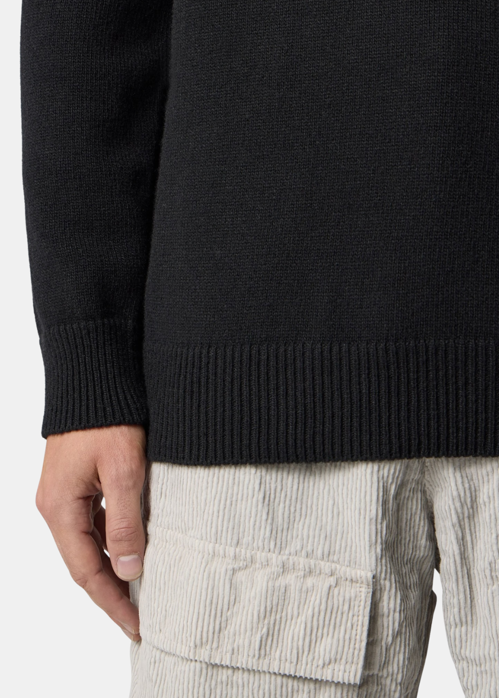 Zoom sur le bas côtelé du pull noir en laine d'agneau Stone Island et le haut d'un pantalon beige en velours côtelé.