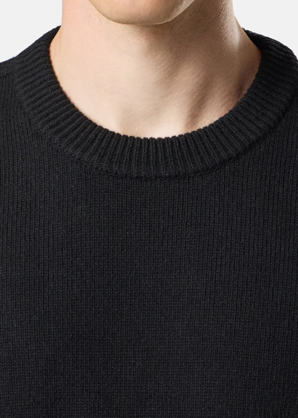 Gros plan sur le col rond tricoté en côtes d'un pull noir Stone Island porté par un mannequin.