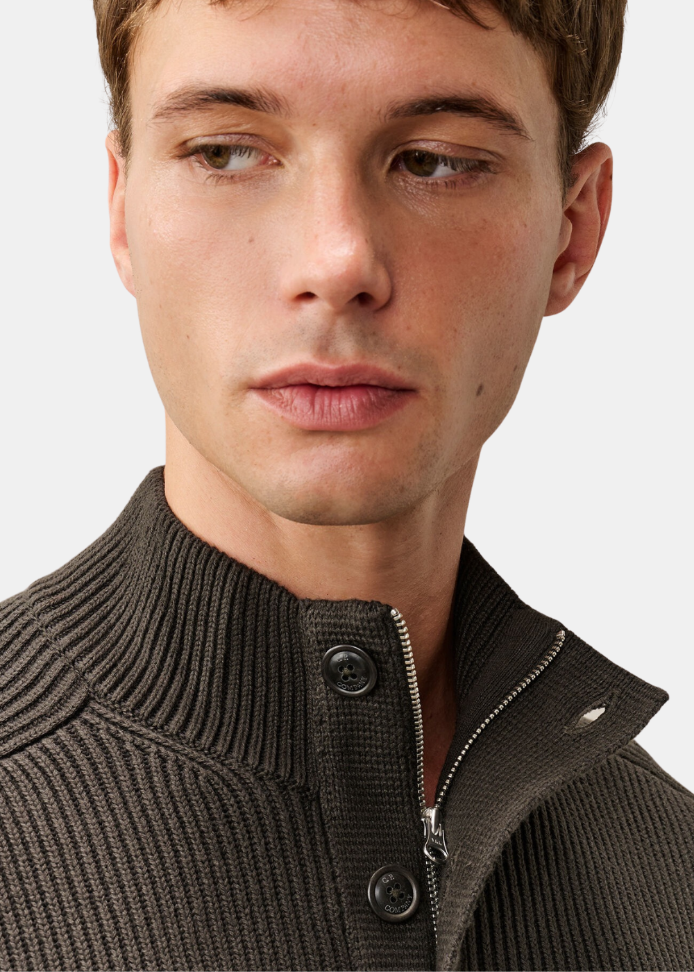 Gros plan sur le col montant boutonné et la fermeture zippée du pull polo C.P. Company gris