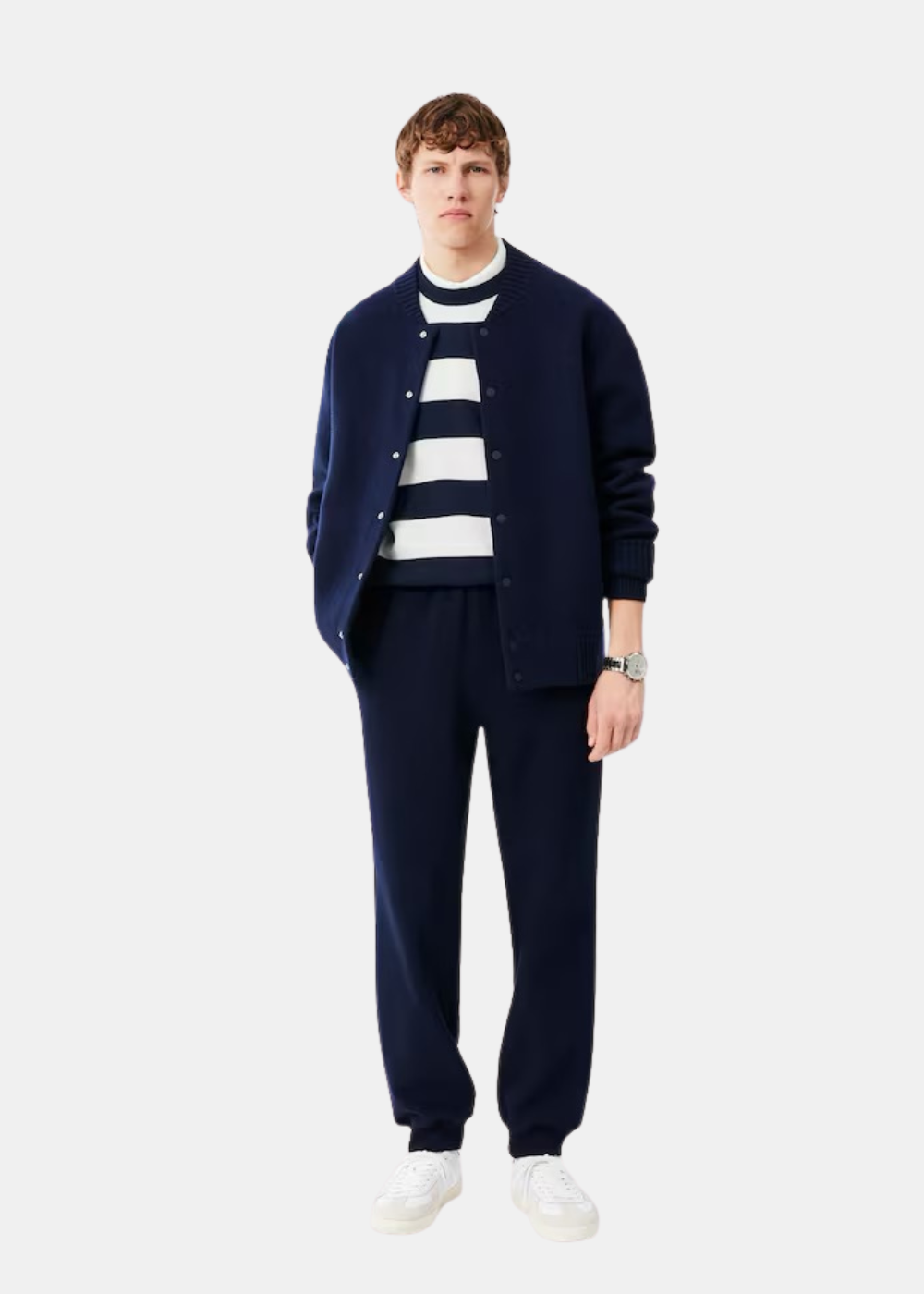 Mannequin homme portant le pull rayé Lacoste sous un cardigan marine, avec pantalon assorti et baskets blanches