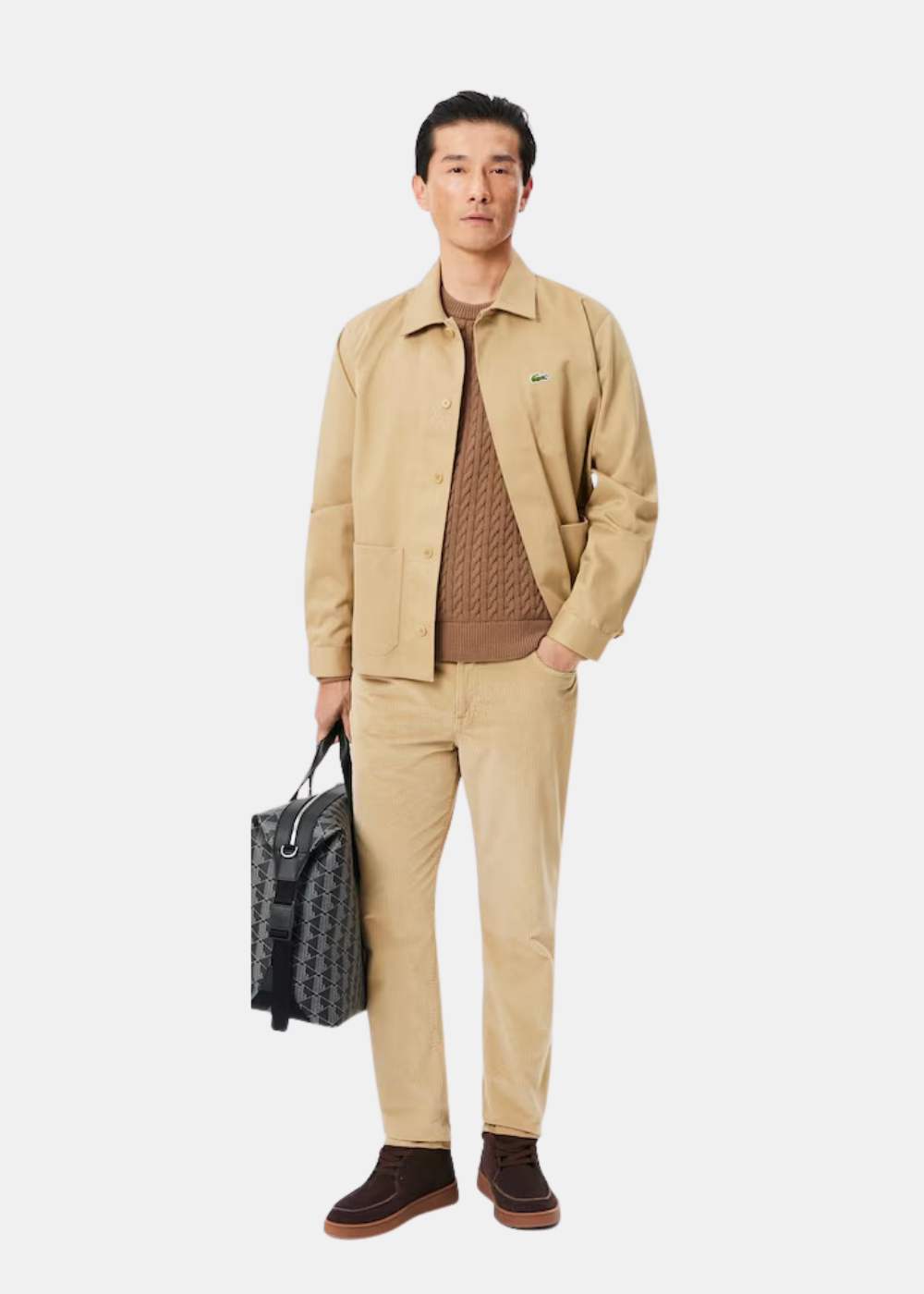 Mannequin homme portant le pull torsadé marron avec une veste beige, un pantalon velours et un sac