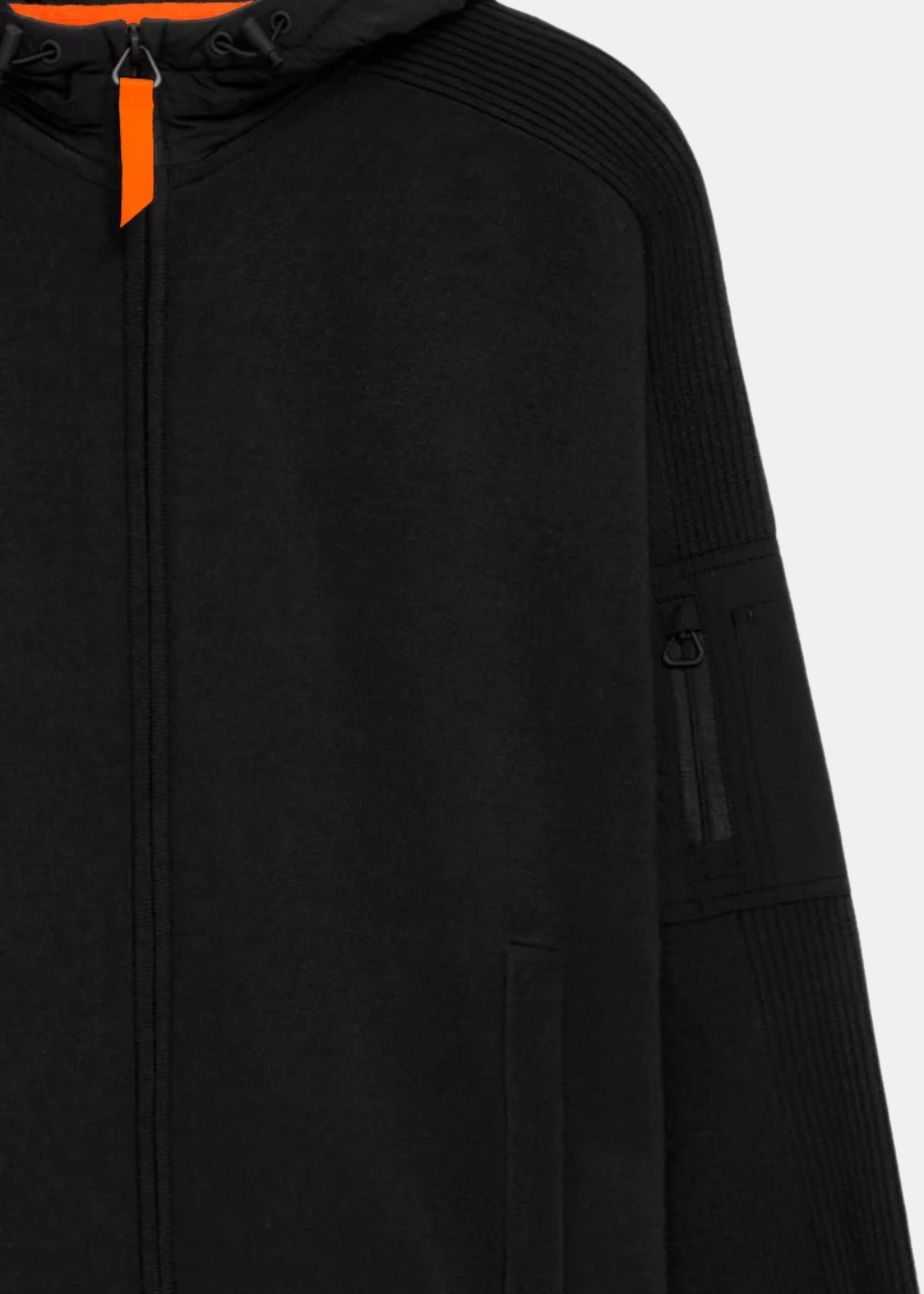 Gros plan sur le pull zippé noir Gertrude montrant la poche zippée sur le bras, la tirette orange du zip central et la texture de la laine tissée