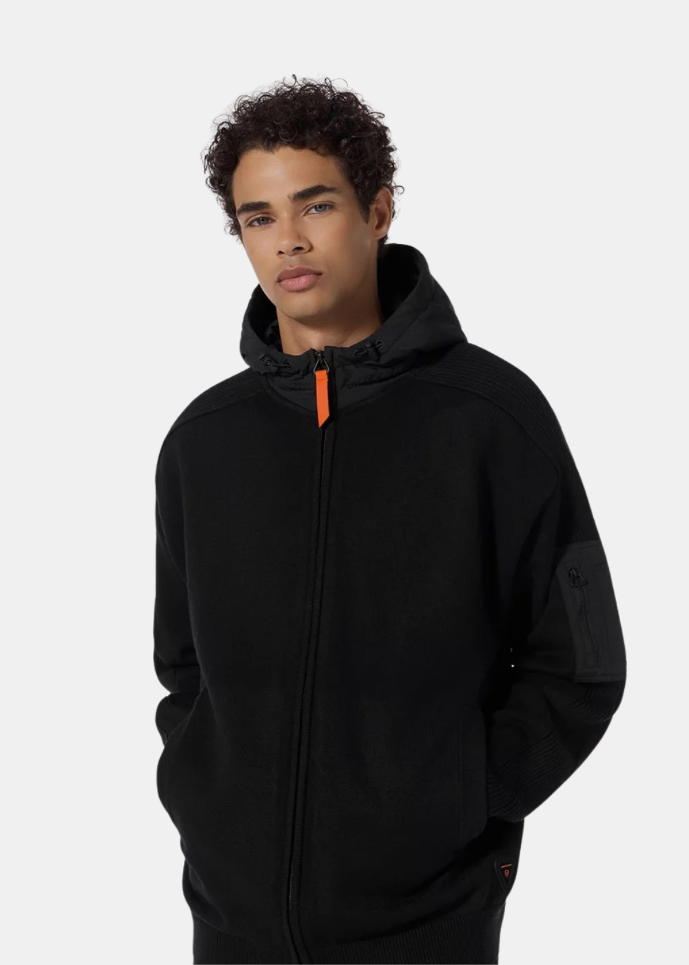 Mannequin homme de face portant le pull zippé à capuche noir Gertrude avec tirette orange contrastante et mains dans les poches