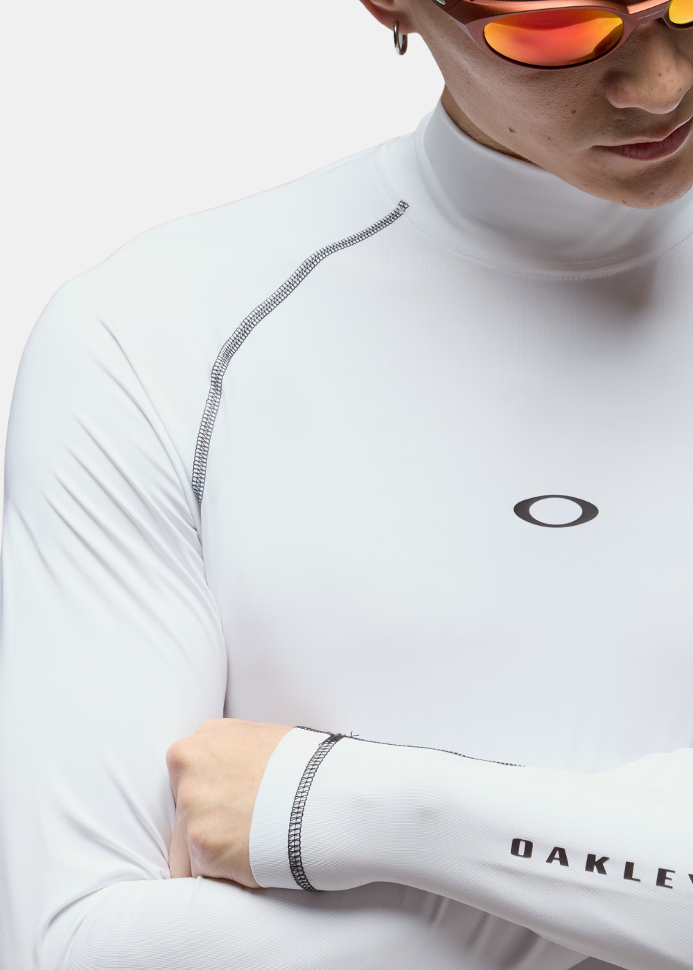 Zoom sur les coutures contrastées noires et le logo sur la poitrine d'un rashguard blanc Oakley porté.