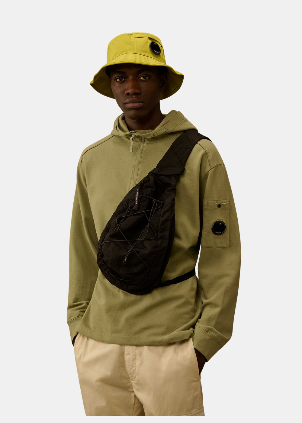 Mannequin portant le sac bandoulière noir C.P. Company en travers du buste sur un sweat olive.