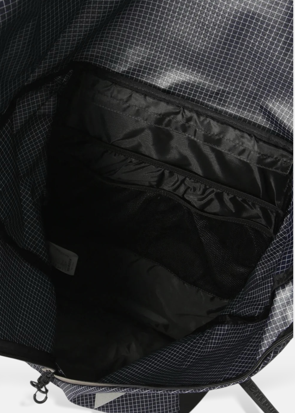Gros plan sur l'intérieur du sac à dos And Wander, montrant les poches de rangement et le tissu quadrillé.