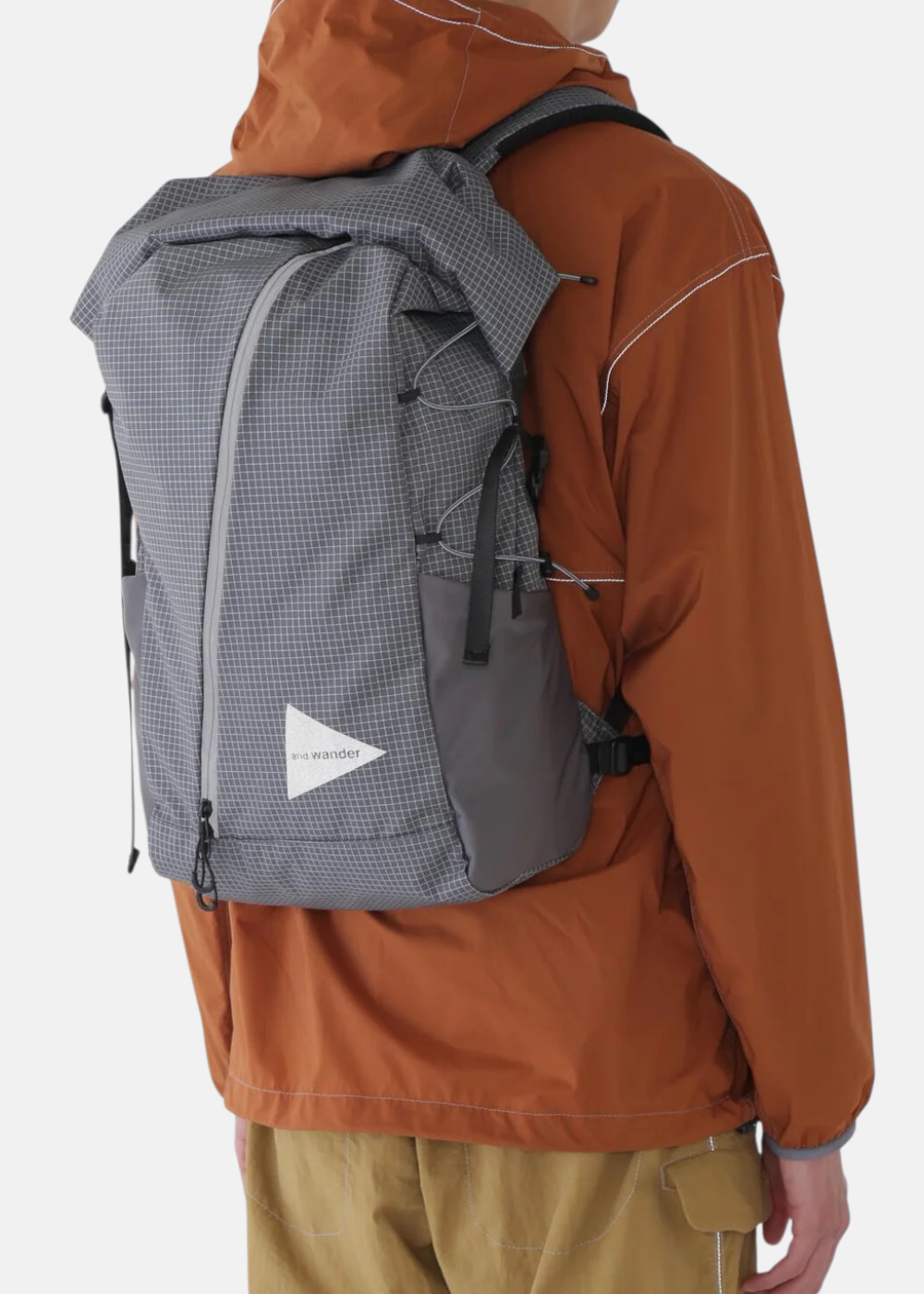 Homme portant le sac à dos And Wander gris, vue de dos montrant le motif quadrillé et les bretelles.