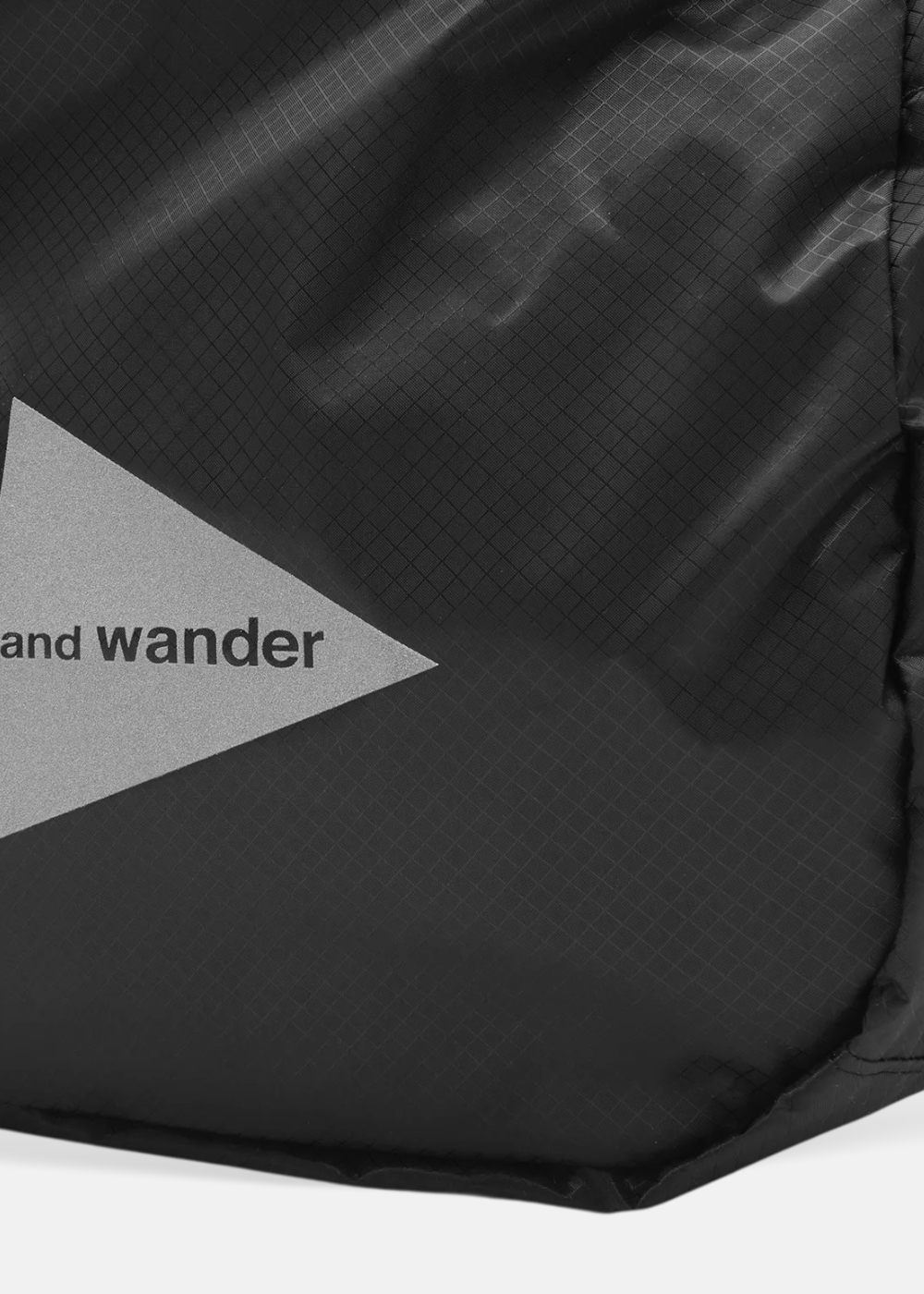 Gros plan sur le logo triangulaire réfléchissant And Wander appliqué sur le tissu quadrillé noir du sac