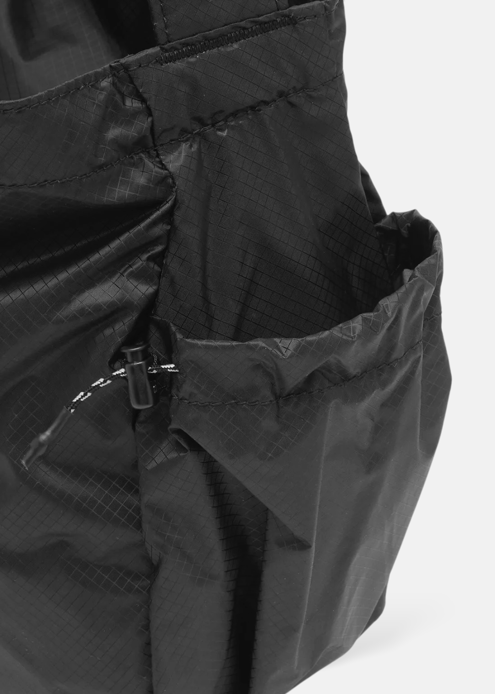 Gros plan sur la poche latérale à cordon de serrage d'un sac noir And Wander en toile Cordura