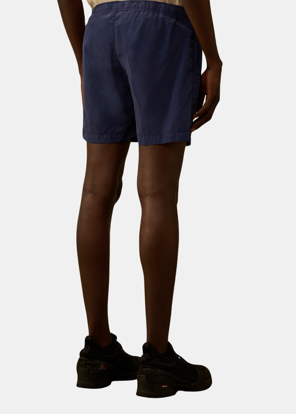 Mannequin homme vu de dos portant le short de bain bleu marine C.P. Company, montrant la coupe ajustée, la longueur mi-cuisse et les détails des finitions sur le nylon Flatt mat