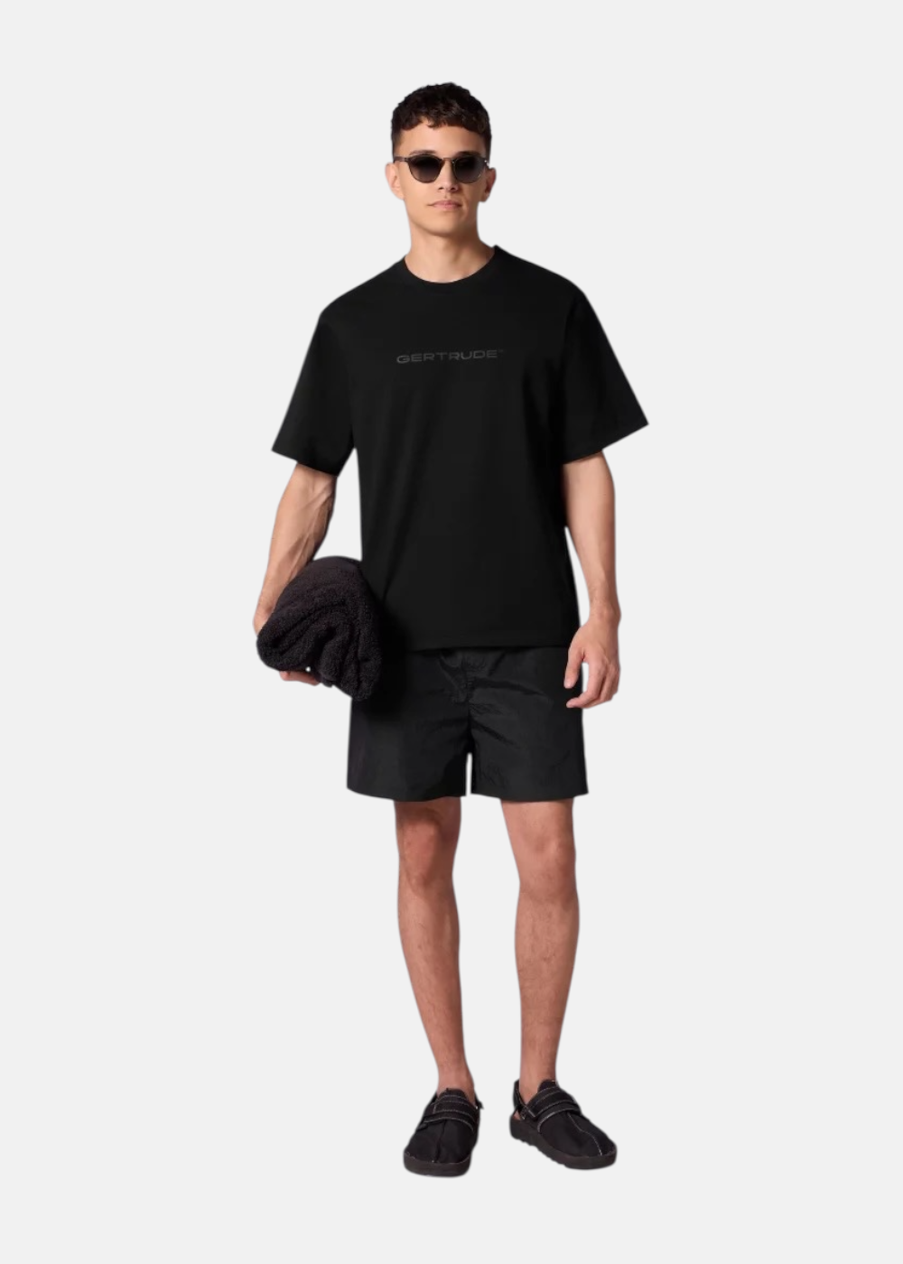 Look complet homme avec short de bain noir Gertrude, t-shirt noir assorti, lunettes de soleil et sandales.