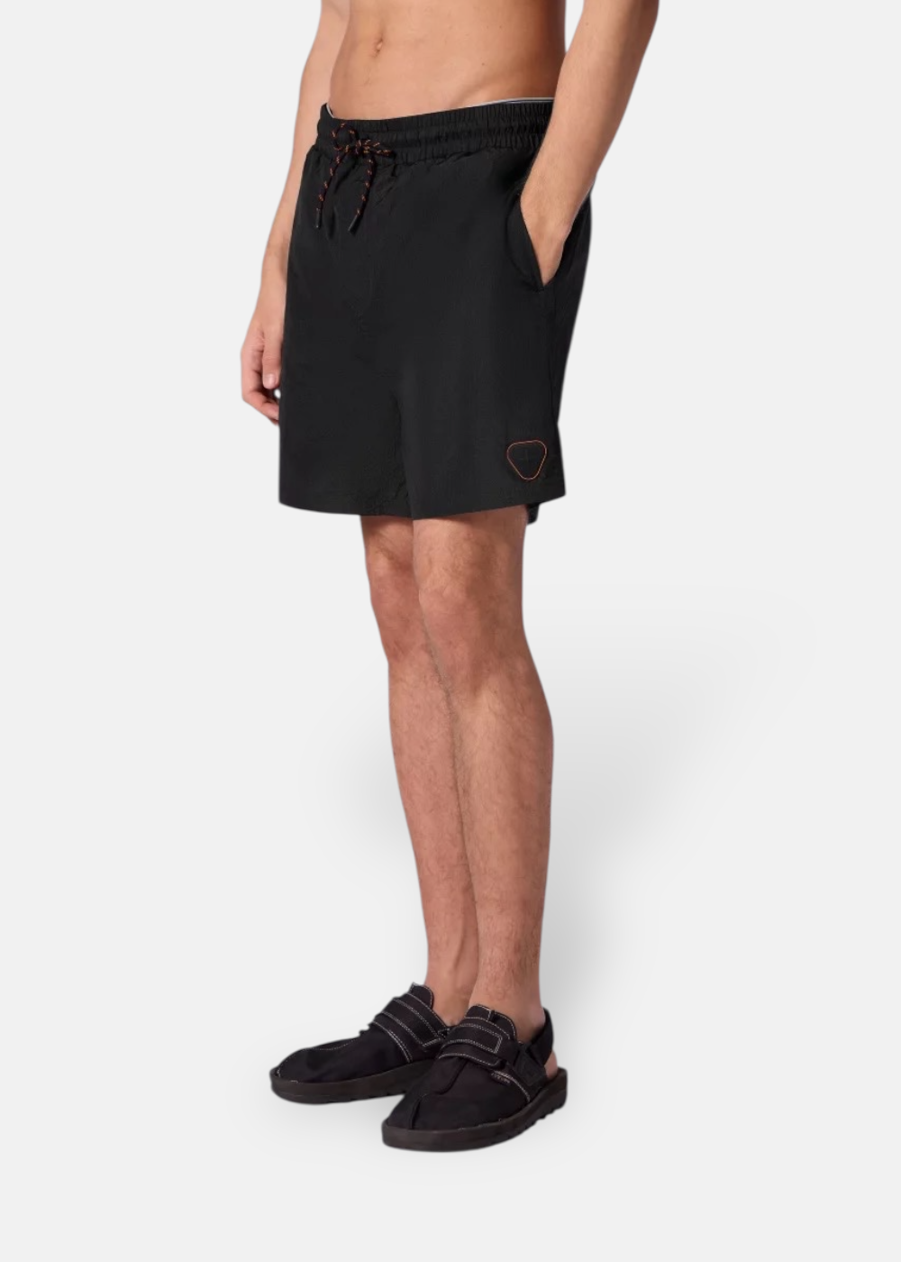 Gros plan de profil d'un homme portant le short de bain noir Gertrude avec poche latérale et écusson.