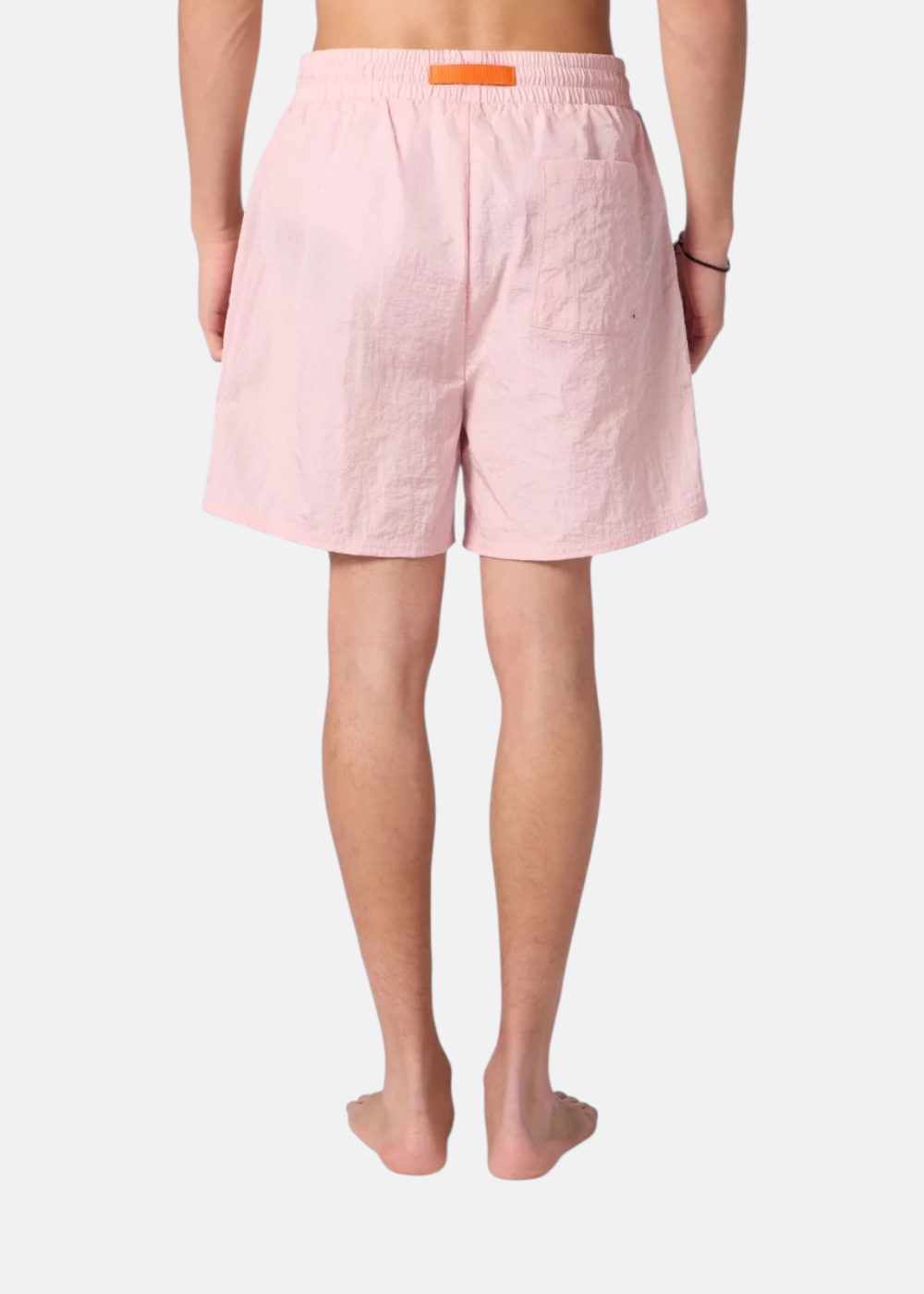 Vue de dos d'un homme portant le short de bain rose Gertrude avec étiquette orange distinctive à la taille.