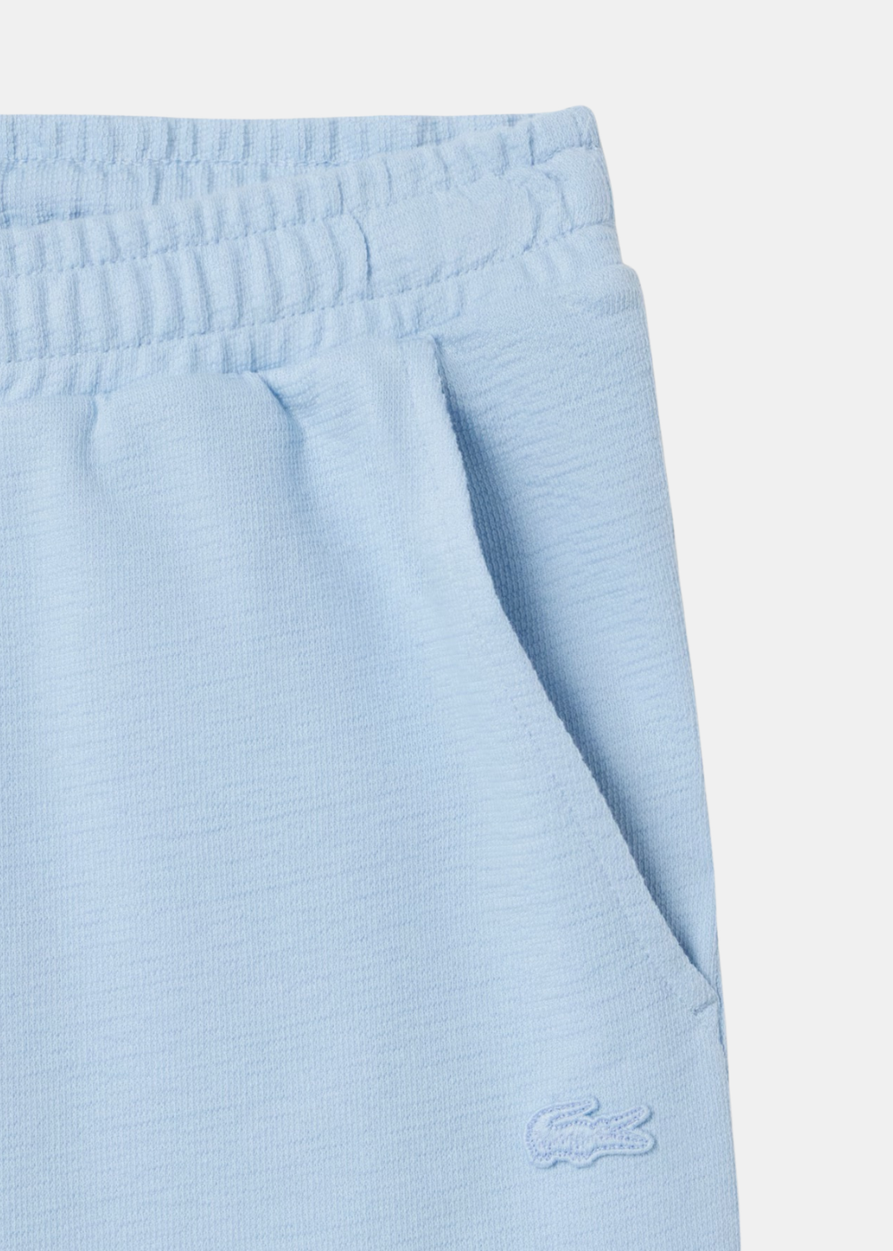 Gros plan sur le jersey texturé bleu clair, la ceinture élastique et le logo crocodile brodé Lacoste