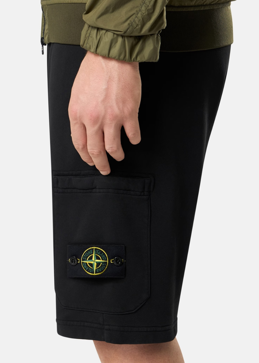 Zoom sur le badge boussole Stone Island boutonné sur la poche latérale d'un short cargo noir porté.