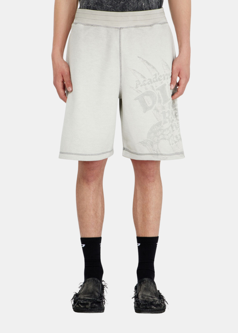 Gros plan de face sur un mannequin portant le short gris dévoré Diesel, soulignant sa coupe droite confortable arrivant au-dessus du genou, associé à des chaussettes hautes noires et des mocassins noirs usés