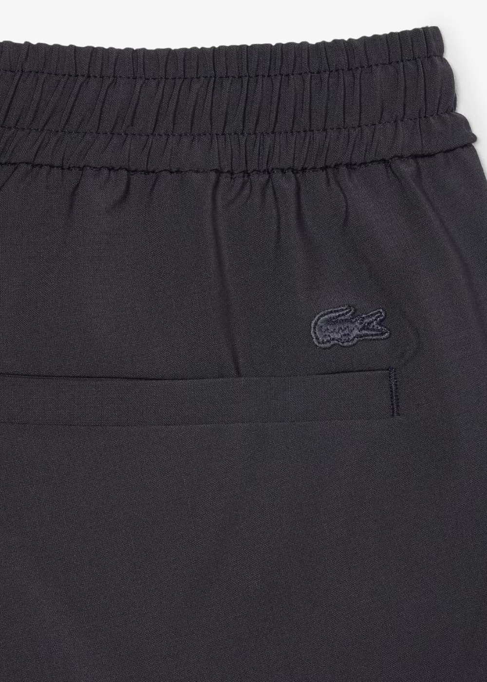 Détail du logo crocodile Lacoste brodé en ton sur ton près de la poche arrière du short gris.