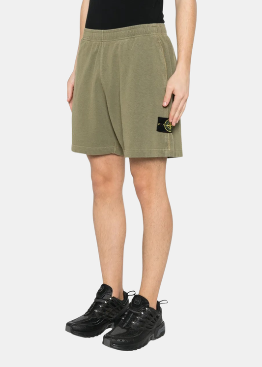 Vue de trois quarts face d'un short kaki délavé Stone Island porté avec des baskets noires, badge boussole visible.