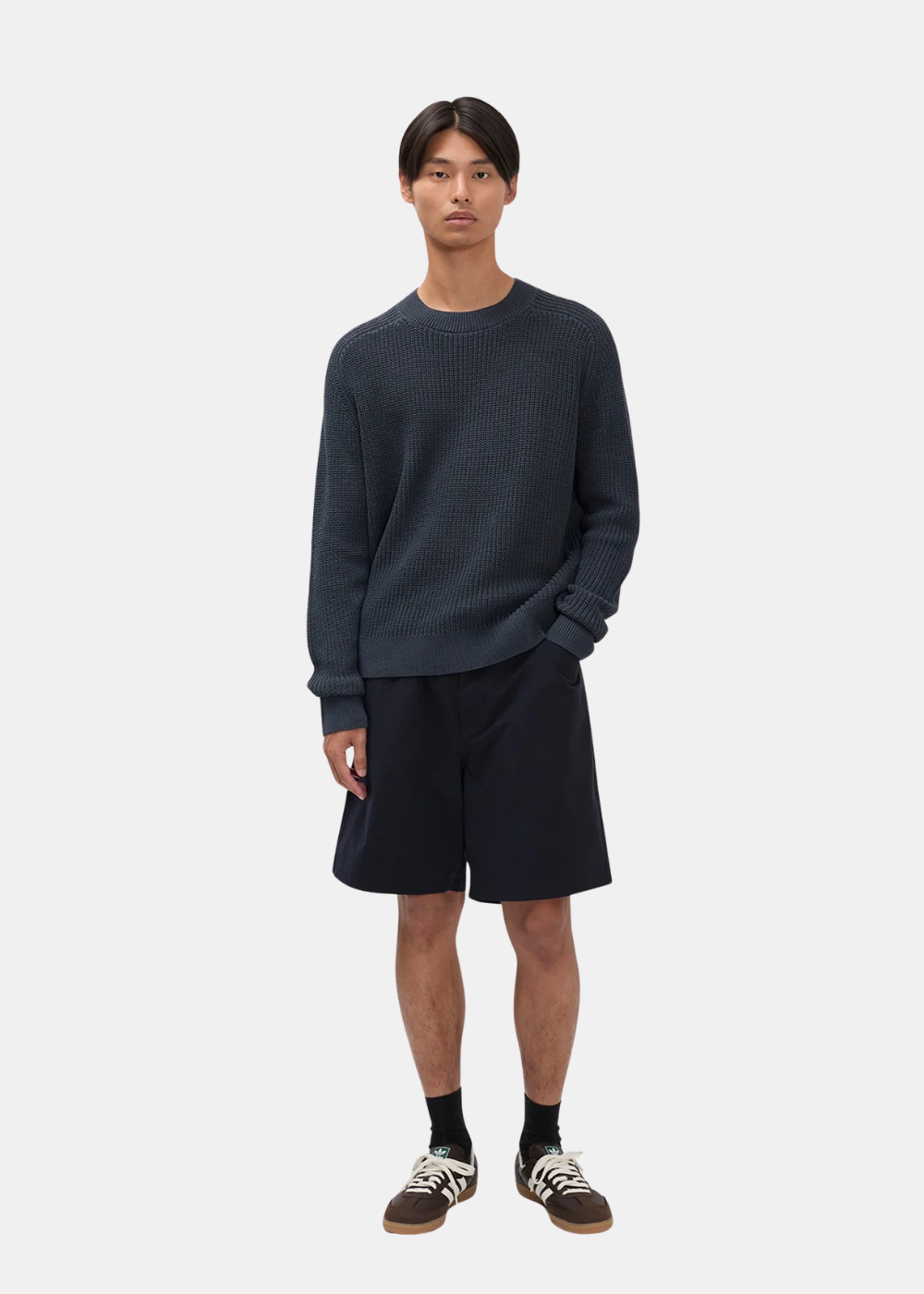 Mannequin homme portant le short technique marine Norse Projects avec un pull en maille gris foncé et des baskets marron.