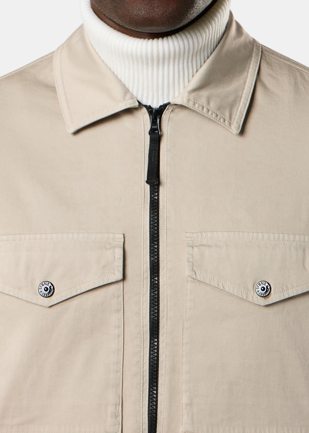 Gros plan de face mettant en valeur le col classique, la fermeture zippée noire et les poches poitrine à rabat boutonné d'une surchemise beige.
