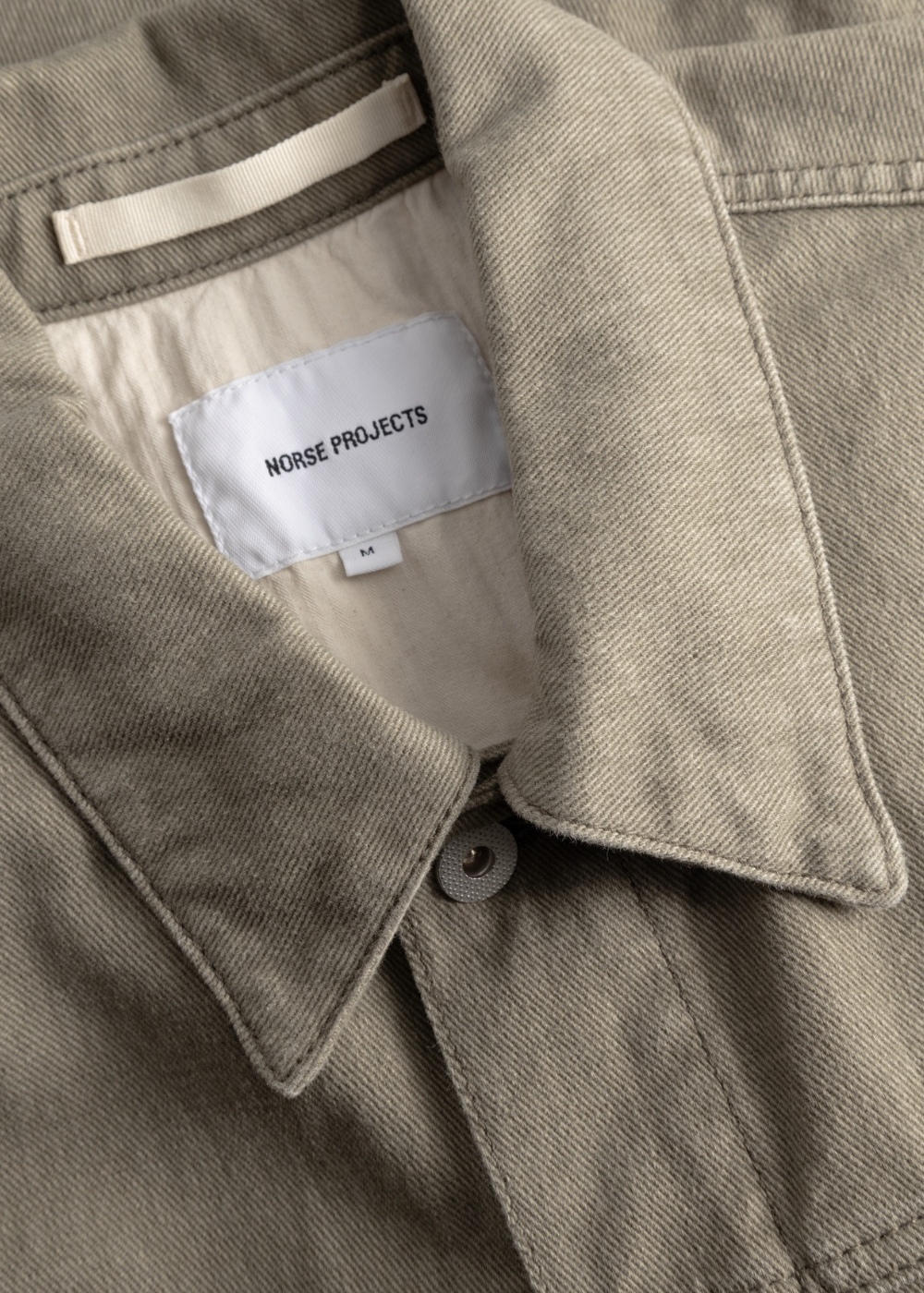 Gros plan sur le col et l'étiquette intérieure Norse Projects de la surchemise homme kaki en coton texturé.