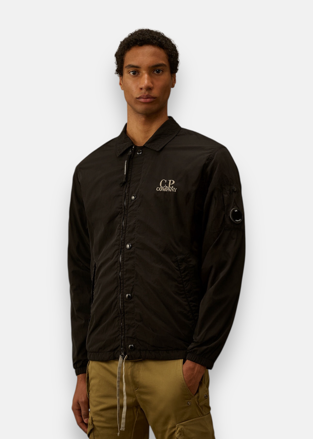 Gros plan du buste d'un homme portant la surchemise noire avec logo brodé et poche Lens sur la manche.