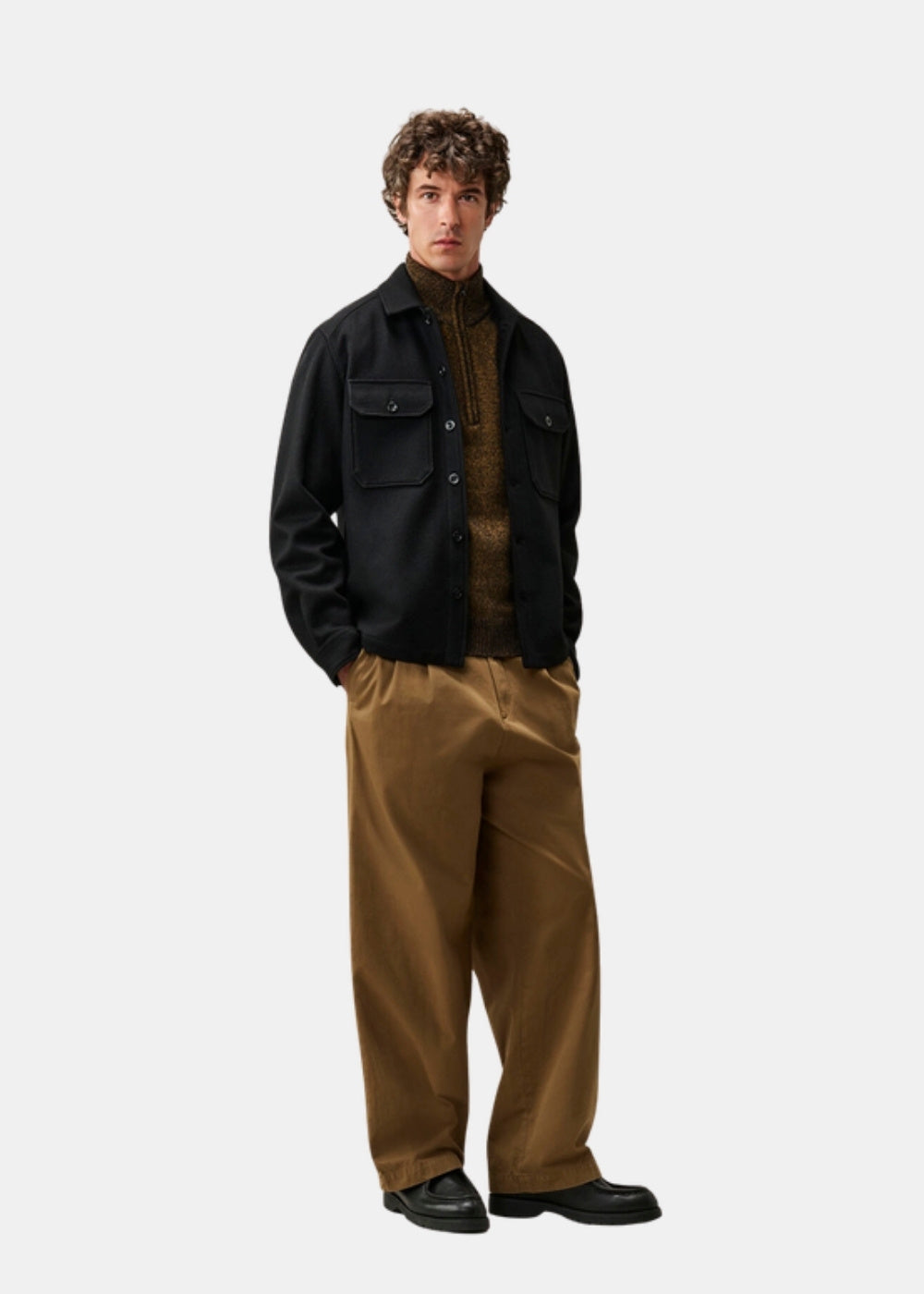 Porté en pied d'une surchemise noire C.P. Company en laine feutrée, ouverte sur un col roulé et un pantalon large camel.