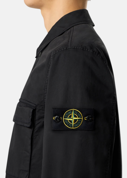 Zoom sur le badge Stone Island boutonné sur la manche gauche d'une surchemise noire portée